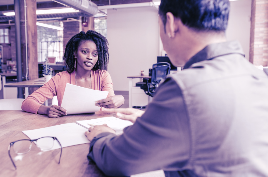 Woman handing document across table during professional interview or review meeting in modern office setting.